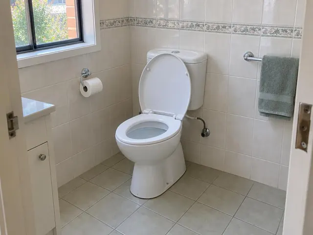 Clean white toilet in a tiled bathroom with a window, towel rail and tiled floor in Chatswood