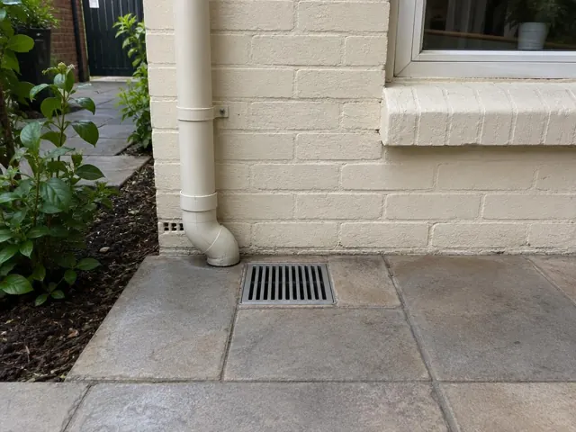 Outdoor grated gully beside a cream brick wall and tiled paving in Lane Cove